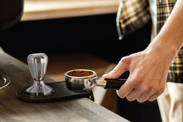 Barista presses ground coffee using tamper. Professional barista working makeing coffee with coffee machine. Hot pouring drink concept. Toned picture